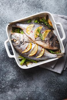 Baked fish dorado with green asparagus in white ceramic baking pan on gray rustic concrete background, top view. Healthy dinner with fish concept, dieting and clean eating .