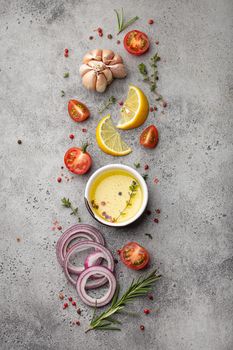 Food cooking ingredients arranged on grey stone rustic table with healthy vegetables, herbs, spices, olive oil from above