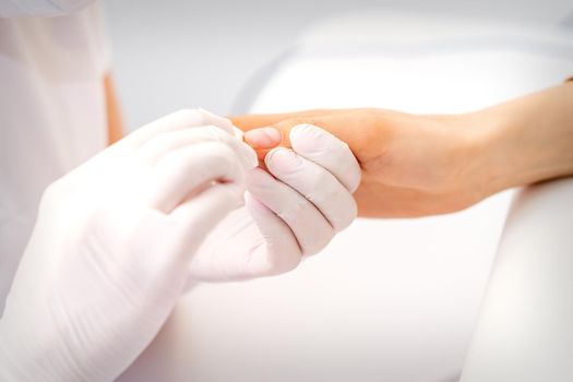 Manicure master wiping the moisturizer from the end of female fingers in beauty salon