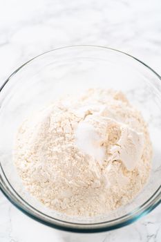 Mixing dry ingredients with a hand whisk in a large glass mixing bowl to bake mini Easter bread kulich.