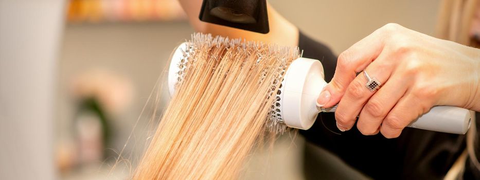 Professional hairdresser dry hair with a hairdryer and round hairbrush in a beauty salon