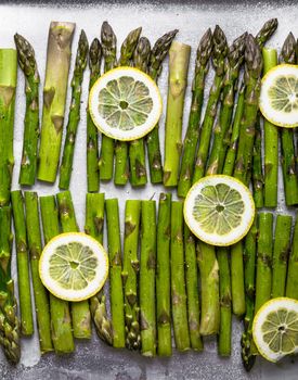 Close-up of fresh green asparagus. Bunch of organic asparagus with lemon ready for cooking on baking tray sprinkled with olive oil and seasonings, good for healthy dieting, top view, close up.