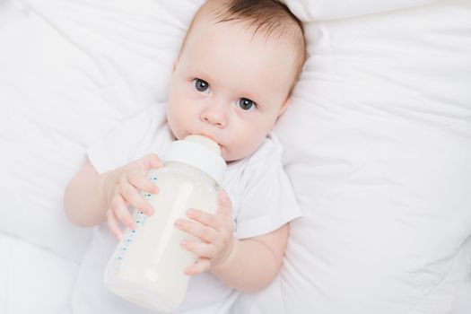 The baby in his crib eats from a bottle . Baby food copyspace . Artificial feeding. Kid top view