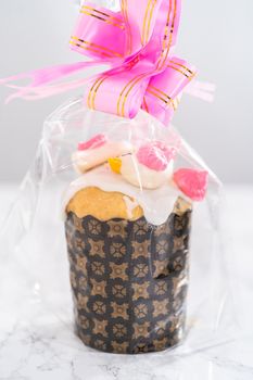 Wrapped mini Easter bread kulich with lemon glaze, decorated with sprinkles and meringue bird-shaped cookies as a good gift.