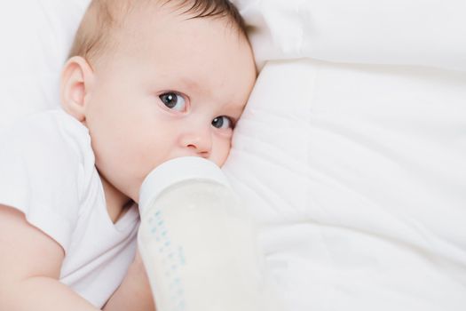 The baby in his crib eats from a bottle . Baby food copyspace . Artificial feeding. Kid top view