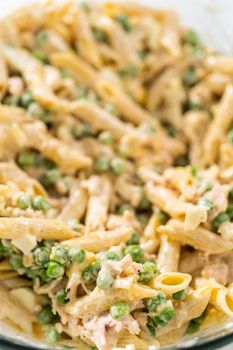 Mixing ingredients in a large glass mixing bowl to make macaroni salad with chicken.