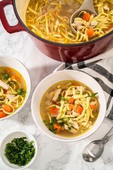 Serving chicken noodle soup with kluski noodles in white ceramic soup bowls.