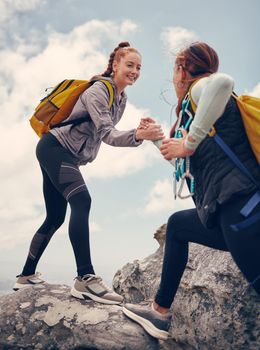 Hiking, help and friends out on a rock or mountain climbing adventure for fitness, exercise and adrenaline. Happy women with support, travel and assistance while out on cliff and reaching the summit.