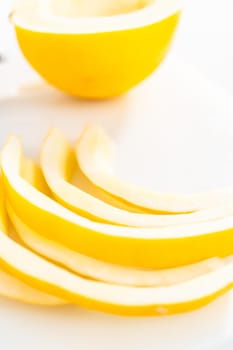 Slicong golden dewlicious melon on a white cutting board.