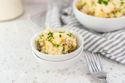 Serving potato salad garnished with fresh parsley in a white ceramic bowl.