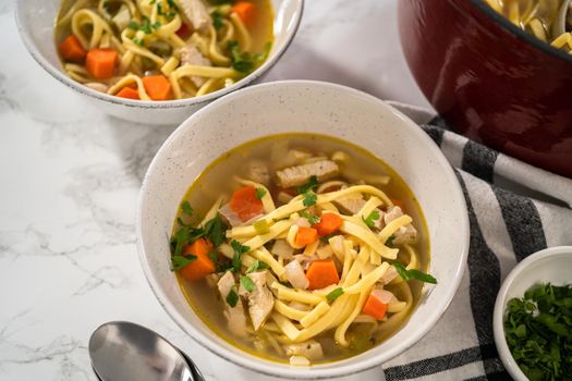 Serving chicken noodle soup with kluski noodles in white ceramic soup bowls.