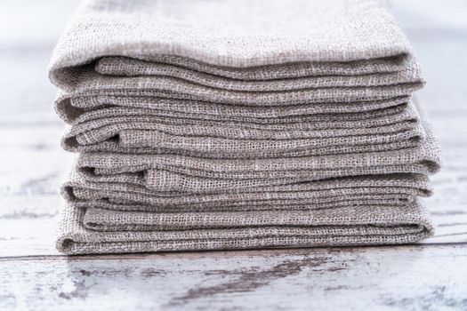 Closeup view of a natural color linen dinner napkin on a wooden white table.