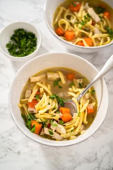 Serving chicken noodle soup with kluski noodles in white ceramic soup bowls.