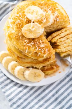 Eating freshly baked coconut banana pancakes garnished with sliced bananas and toasted coconut.