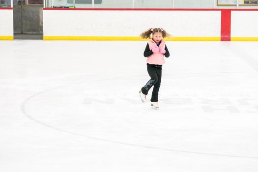 Little girl practicing figure skating moves on the indoor ice rink.