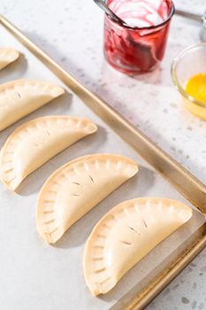 Unbaked sweet cherry empanadas on a baking sheet lined with a parchment paper baking sheet.