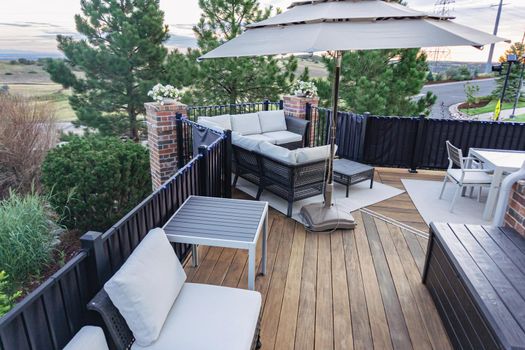 Morning on a summer day. Fully furnished backyard patio with a grill, sitting area, and umbrella.