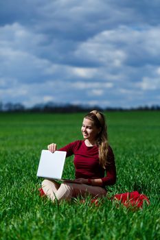 Joyful young girl on the grass with a laptop on her lap. He raised his hands up and laughed. Happiness in the lifestyle of a classical student. Work on the nature. Rest after a good working day.