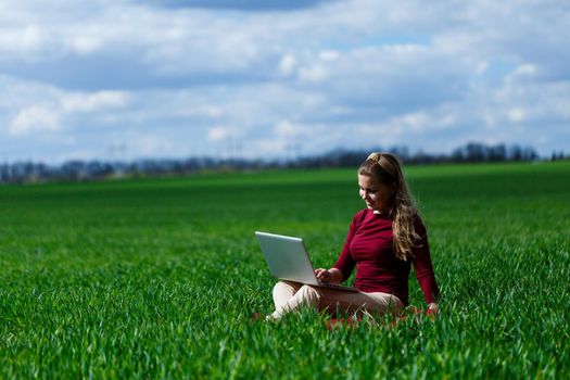 Joyful young girl on the grass with a laptop on her lap. He raised his hands up and laughed. Happiness in the lifestyle of a classical student. Work on the nature. Rest after a good working day.