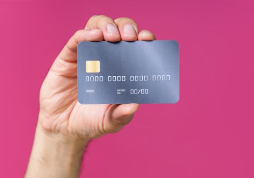 Best offer, dark grey-purple debit, credit card in man hand isolated on pink background. Financial, banking concept. No face visible.