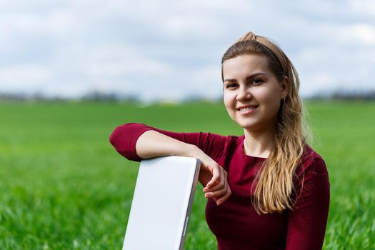 Young successful woman is sitting on green grass with a laptop in her hands. Rest after a good working day. Work on the nature. Student girl working in a secluded place. New business ideas