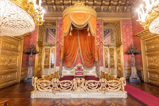 Turin, Italy - Circa August 2021: old throne room interior with chair in luxury palace. Red and gold antique Baroque style - Savoia Royal Palace