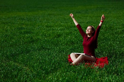 Young successful woman is sitting on green grass with a laptop in her hands. Rest after a good working day. Work on the nature. Student girl working in a secluded place. New business ideas