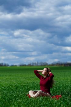 Young successful woman is sitting on green grass with a laptop in her hands. Rest after a good working day. Work on the nature. Student girl working in a secluded place. Workplace in nature