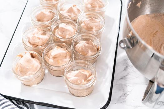 Scooping mixture into the small glass jars to make homemade chocolate ice cream.