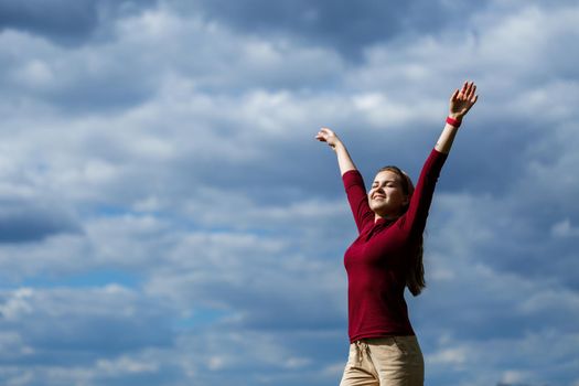 Joyful young girl on a background of the sky with clouds. He raised his hands up and laughed. Happiness in lifestyle. Inspiration in nature. Rest after a good working day.