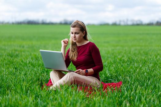 Young successful woman is sitting on green grass with a laptop in her hands. Work on the nature. Student girl working in a secluded place. New business ideas