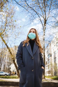 Girl, young woman in a protective sterile medical mask on her face, looking at the camera outdoors, in the spring garden. Air pollution, virus, pandemic coronavirus concept.
