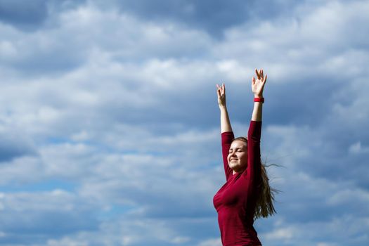 Joyful young girl on a background of the sky with clouds. He raised his hands up and laughed. Happiness in lifestyle. Inspiration in nature. Rest after a good working day.