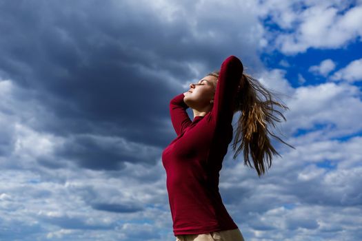 Joyful young girl on a background of the sky with clouds. He raised his hands up and laughed. Happiness in lifestyle. Inspiration in nature. Rest after a good working day.
