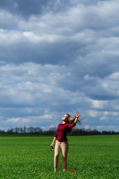 Beautiful young blonde woman stands on green grass in a park. Blue sky with clouds. The girl smiles and enjoys a good day.