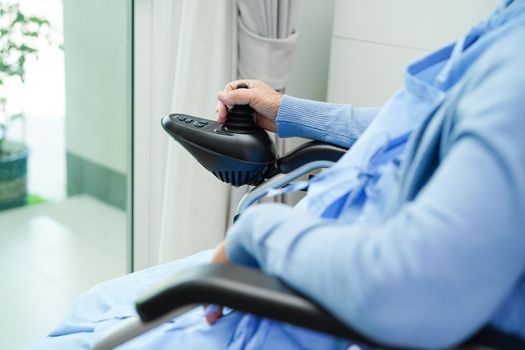 Asian elderly woman disability patient sitting on electric wheelchair in park, medical concept.