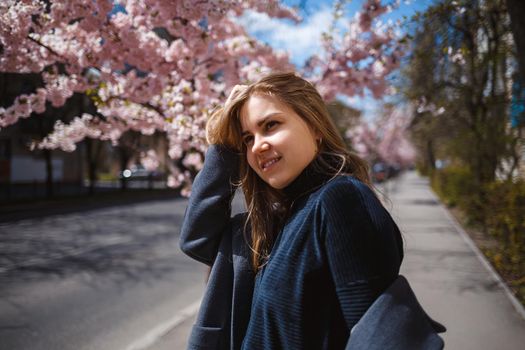 Sakura branches with flowers on a tree on the city streets. Happy woman girl spinning on the street with blooming sakura. Gorgeous fashionable girl outdoors. Sakura tree blossoms.