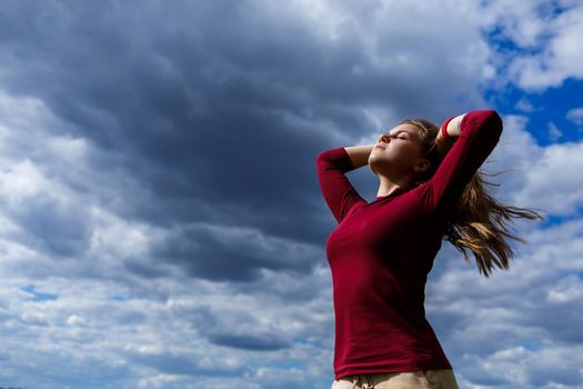 Joyful young girl on a background of the sky with clouds. He raised his hands up and laughed. Happiness in lifestyle. Inspiration in nature. Rest after a good working day.