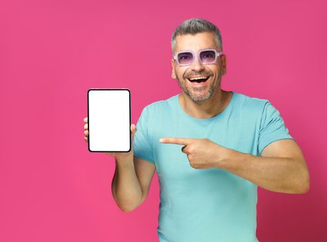 Excited adult man, guy 30s 40s hold huge digital tablet wearing casual blue shirt and sunglasses isolated on pink background. Man with phone studio shot. Mobile app advertisement.