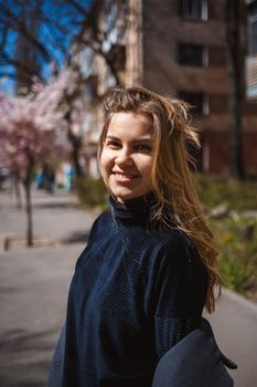 Sakura branches with flowers on a tree on the city streets. Happy woman girl spinning on the street with blooming sakura. Gorgeous fashionable girl outdoors. Sakura tree blossoms.