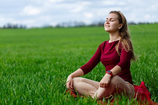 Beautiful woman is sitting on the grass and resting. The girl closed her eyes and enjoyed the sun. She smiles and enjoys a warm day.