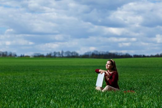 Young successful woman is sitting on green grass with a laptop in her hands. Rest after a good working day. Work on the nature. Student girl working in a secluded place. Workplace in nature