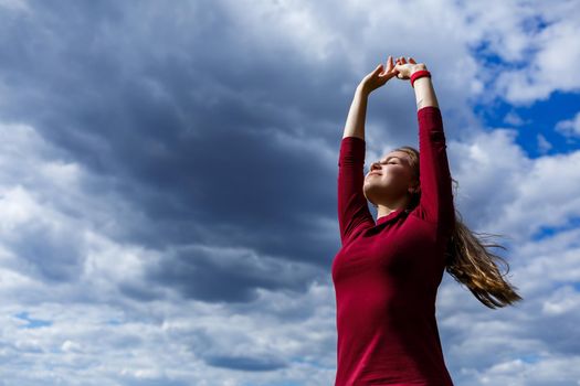 Joyful young girl on a background of the sky with clouds. He raised his hands up and laughed. Happiness in lifestyle. Inspiration in nature. Rest after a good working day.
