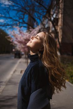 Sakura branches with flowers on a tree on the city streets. Stylish woman girl runs on the street with blooming sakura. Gorgeous fashionable girl outdoors. Sakura tree blossoms.
