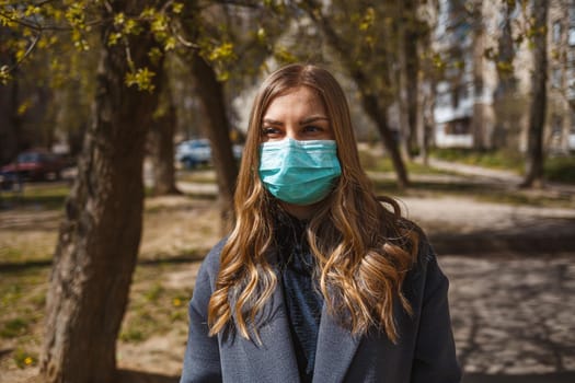 Girl, young woman in a protective sterile medical mask on her face, looking at the camera outdoors, in the spring garden. Air pollution, virus, pandemic coronavirus concept.