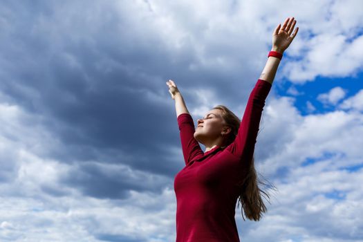 Joyful young girl on a background of the sky with clouds. He raised his hands up and laughed. Happiness in lifestyle. Inspiration in nature. Rest after a good working day.