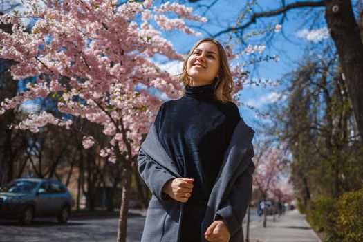 Sakura branches with flowers on a tree on the city streets. Happy woman girl spinning on the street with blooming sakura. Gorgeous fashionable girl outdoors.