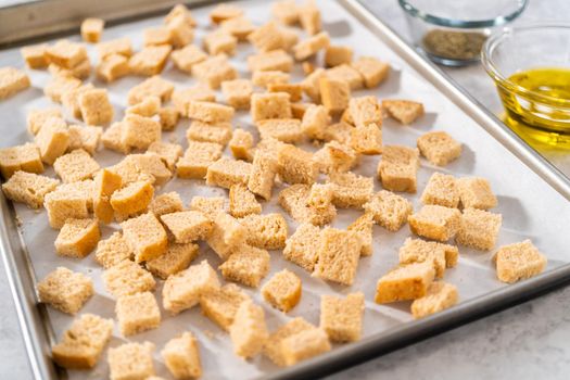 Baking croutons seasoned with olive oil and spiced on a baking sheet lined with parchment paper.