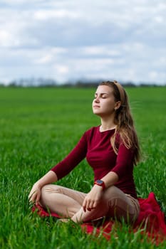 Beautiful woman is sitting on the grass and resting. The girl closed her eyes and enjoyed the sun. She smiles and enjoys a warm day.