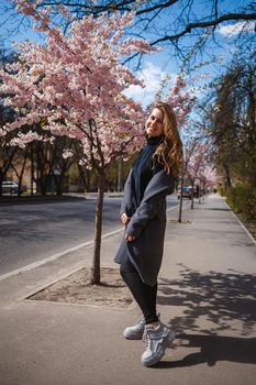 Sakura branches with flowers on a tree on the city streets. Happy woman girl spinning on the street with blooming sakura. Gorgeous fashionable girl outdoors. Sakura tree blossoms.